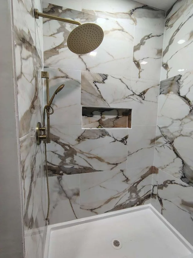 Marble-tiled walk-in shower with brass rain head and recessed niche in a custom home built in Grove, Oklahoma